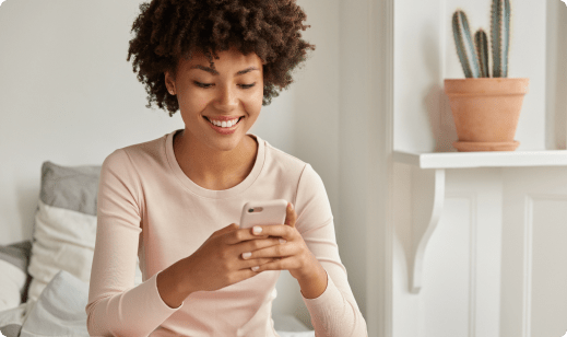positive black lady with afro haircut holds modern cellular reconsiders text message recieved from friend types feedback dressed nightclothes sits comfortable bed alone has lazy day
